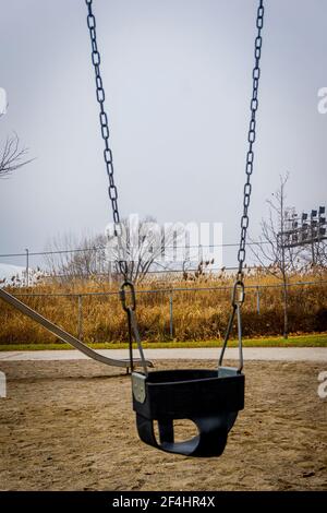 Un'oscillazione vuota in un parco giochi deserted può illustrare un covid situazione di blocco in cui i bambini non sono ammessi nel parco giochi Foto Stock