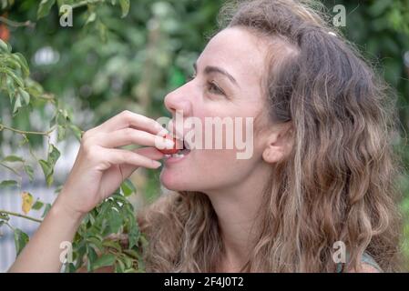Donna bionda che mangia pomodoro. Donna che si nuda in giardino. Cibo naturale. Stile di vita. Brasiliani mangiare verdure appena selezionate. Disintossicazione e cibo naturale. Foto Stock