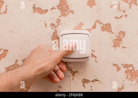 La mano dell'uomo spegne la luce con un interruttore elettrico su uno sfondo interno moderno. Foto Stock