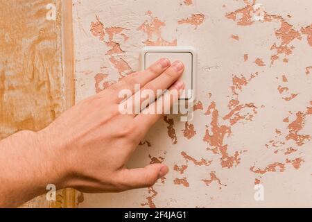 La mano dell'uomo spegne la luce con un interruttore elettrico su uno sfondo interno moderno. Foto Stock