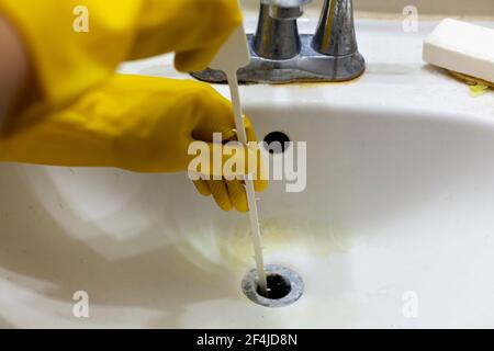 Una persona sta cercando di sbloccare lo scarico di un lavello utilizzando uno strumento di plastica usa e getta a coclea del serpente che aiuta a tirare i capelli e i residui di sapone dal sinkhole. Cl Foto Stock