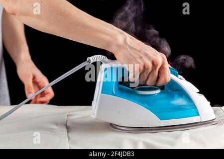 Primo piano immagine isolata di una donna bianca che stira un panno su un'asse da stiro. Dal ferro fuoriesce vapore caldo su sfondo scuro. Donna che fa Foto Stock