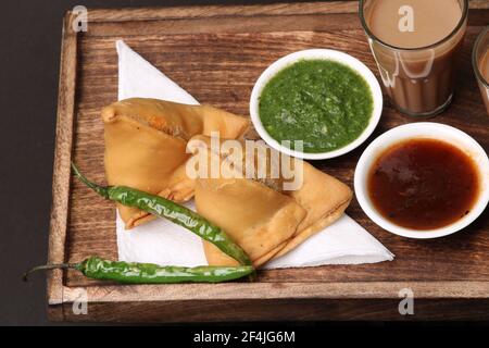 Snack indiano in casa speziato e deliziosa samosa servita con verde, tamarindo chutney taglio tè masala, chai, Foto Stock