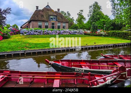 Giethoorn, Paesi Bassi - 6 luglio 2019: Barche rosse attraccate nel canale di fronte ad una tipica casa rurale olandese nel villaggio di Giethoorn, Paesi Bassi Foto Stock