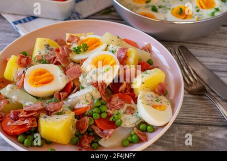 Delizioso piatto d'uovo con uova sode a metà, prosciutto fritto, verdure, patate in una gustosa salsa di bechamel alle erbe servita su un piatto sul tavolo da cucina Foto Stock