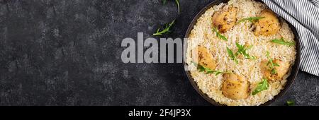 Riso con cosce di pollo, pilaf in padella su fondo scuro. Vista dall'alto, sopra, spazio di copia Foto Stock