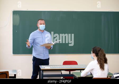 Studenti in maschere protettive che studiano in classe con insegnante. Precauzioni nella pandemia del coronavirus Foto Stock