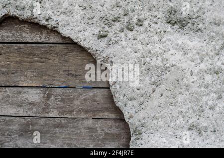 Calcestruzzo e vecchie tavole di legno. Un foro in una recinzione grigia con bordi irregolari è stato patchato con le tavole. Attraverso le fessure tra le barre. Muschio su un cemento Foto Stock
