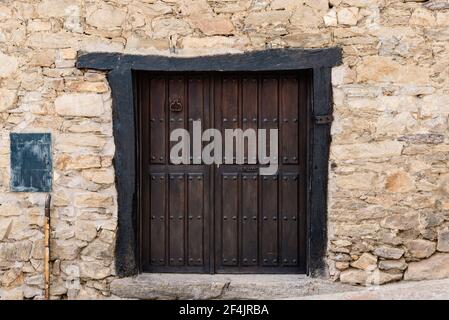 Vecchia porta di legno in pietra muro in casa tradizionale in Il villaggio di Horcajuelo de la Sierra a Madrid Foto Stock