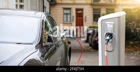 Primo piano di un'auto elettrica con un cavo collegato e. una stazione di ricarica Foto Stock