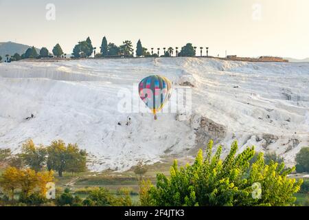 Bella mongolfiera colorata sullo sfondo delle montagne bianche di Pamukkale in Turchia. Cascata di bagni terrazzati con stalattiti di calcite. Foto Stock