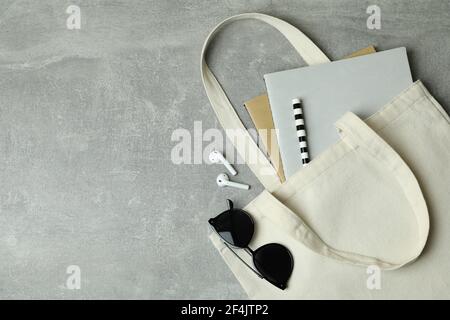 Borsa ecologica con copybook, cuffie e occhiali da sole su sfondo grigio Foto Stock