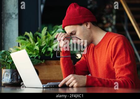 Uomo stanco che prende una pausa durante il lavoro online sul laptop, tenendo la testa in mano, sensazione di mancanza di energia. Foto Stock