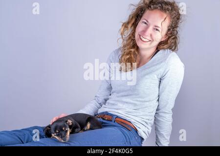 Dettaglio di una bella donna con occhiali e capelli ricci marroni, seduta sorridente con un cucciolo Jack Russell Terrier sulle gambe Foto Stock