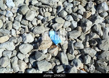 Maschera medica utilizzata per la protezione COVID gettata sulla spiaggia conseguente inquinamento della natura e problemi di ecologia Foto Stock