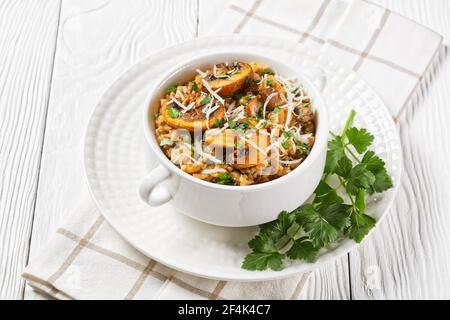 classico risotto cremoso ai funghi cosparso di parmigiano grattugiato e prezzemolo in una ciotola bianca, primo piano, cucina italiana Foto Stock