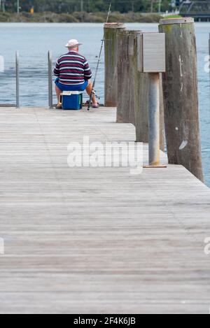 Un vecchio pescatore solista si siede su un Esky refrigeratore e. Pesci da un pontile a Narooma nel nuovo Sud Galles costa sud in Australia Foto Stock