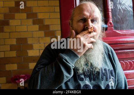 Tilburg, Paesi Bassi. Senior maschio adulto con barba di fumare un cigerette vicino alla porta di ingresso di un ristorante cafe. Foto Stock