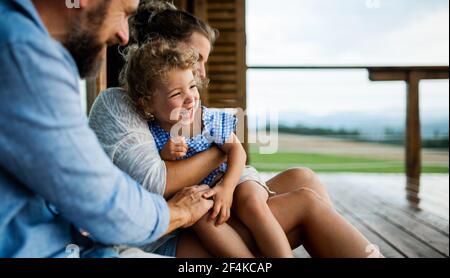 Famiglia con piccola figlia seduta sul patio di cabina di legno, vacanza in natura concetto. Foto Stock