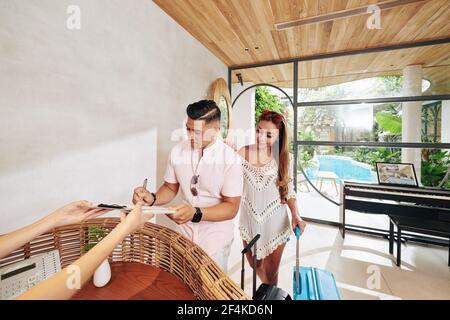 Uomo che riempie il documento per lui e sua moglie quando si è in piedi presso la reception dell'hotel termale Foto Stock