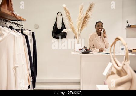 Sorridente imprenditore africano che parla al telefono in lei negozio Foto Stock