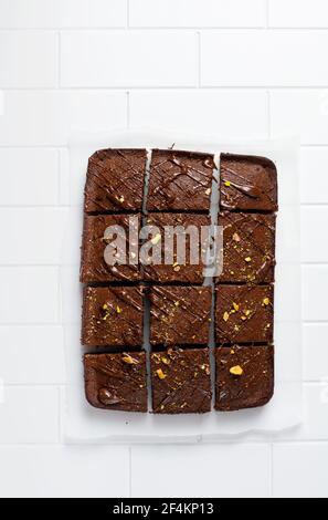 Quadrati di cioccolato con pistacchio e fragole su carta bianca su sfondo chiaro, vista dall'alto, composizione orizzontale. Cibo piatto Foto Stock