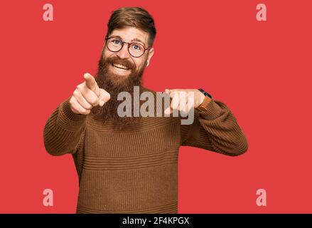 Giovane irlandese rosso uomo che indossa abiti casual e occhiali che punta a te e la fotocamera con le dita, sorridente positivo e allegro Foto Stock