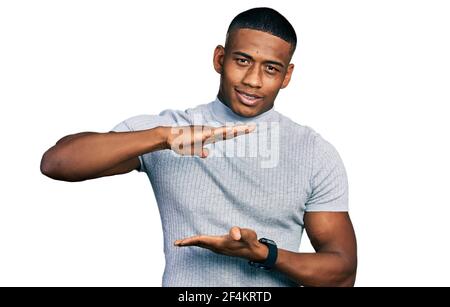 Giovane uomo nero che indossa una t-shirt casual gesturing con le mani che mostrano grande e grande segno di misura, misura simbolo. Sorridendo guardando la fotocamera. Misurazione Foto Stock