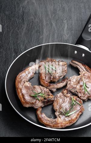 Costolette di agnello in padella su fondo di pietra nera Foto Stock