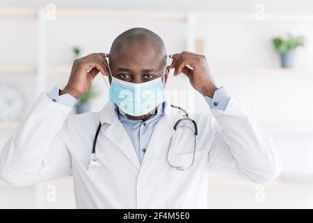 Terapeuta afroamericana maschio che indossa una maschera chirurgica medica per prevenire le infezioni, lavorando in ufficio Foto Stock