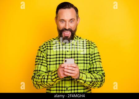 Foto di un uomo maturo eccitato felice positivo sorpreso uso cellulare tipo di chat sms blogger isolato su sfondo giallo Foto Stock