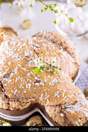 Dessert tradizionali italiani per Pasqua - colomba di Pasqua. Dolci natalizi con mandorle e glassa di zucchero su sfondo chiaro e rami fioriti, decorazioni pasquali e uova. Verticale. Primo piano Foto Stock