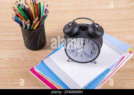 Portamatite pieno di matite colorate con libri e un sveglia nera vintage su un tavolo di legno Foto Stock