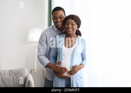 Felice coppia nera incinta coccolare mentre si passa il tempo a casa Foto Stock