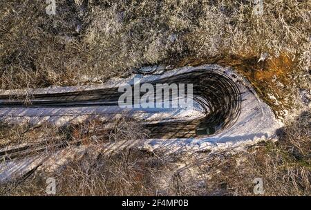 Vista aerea dall'alto di una lussuosa auto sportiva nera che guida sulla tortuosa strada di montagna in inverno. Vista dall'alto di un'auto nera che guida nella neve Foto Stock