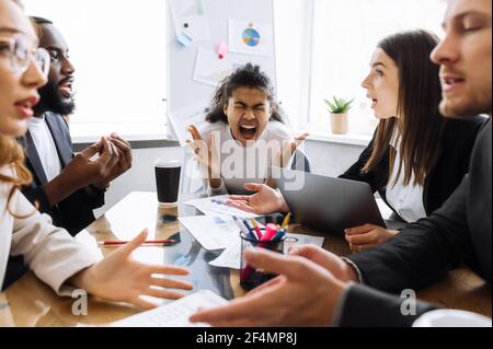 I dipendenti spossati di sesso maschile e femminile non possono raggiungere un accordo, discutendo. Arrabbiato gente di affari che ha un brainstorm teso, capo della donna afroamericana sta gridando, sentendosi frustrato Foto Stock