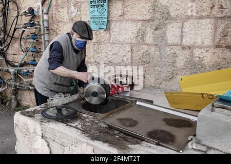 Gerusalemme, Israele. 22 marzo 2021. Un uomo ebreo purifica gli utensili da cucina appena acquistati, immergendoli in una cisterna di acqua piovana nel quartiere di Nachlaot in preparazione della Pasqua, che sarà celebrata quest'anno a partire dal tramonto, il 27 marzo 2017. Il rituale ricco di vacanze impone che gli ebrei rimuovano tutti i prodotti lievitati, hametz, dalle loro cucine e case. Credit: NIR Alon/Alamy Live News Foto Stock