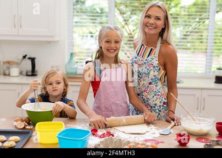 Sorridente madre, figlia e figlio caucasici che indossano grembiuli che cucinano insieme i biscotti in cucina Foto Stock