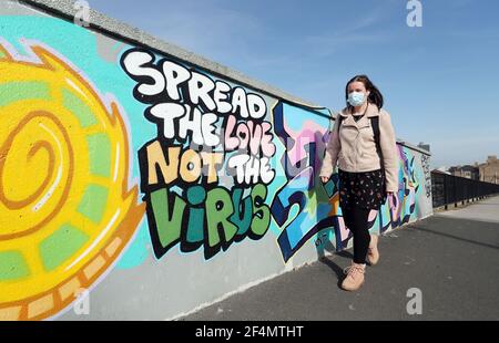 Una donna passa attraverso l'arte di strada che recita "l'amore non il virus" a Hull, nello Yorkshire, durante il terzo blocco nazionale dell'Inghilterra per frenare la diffusione del coronavirus. Data immagine: Lunedì 22 marzo 2021. Foto Stock