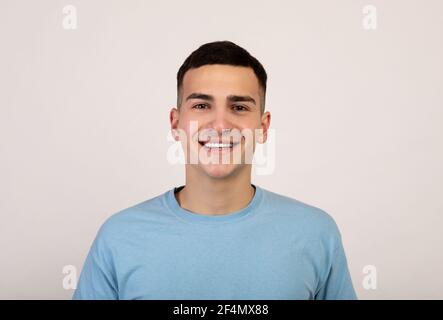 Ritratto di bel giovane caucasico in abiti casual sorridente e guardando la fotocamera su sfondo grigio chiaro Foto Stock
