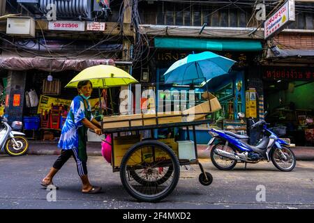 Una venditrice di cibo femminile spinge il suo carrello alimentare lungo la strada a Chinatown, Bangkok, Thailandia Foto Stock