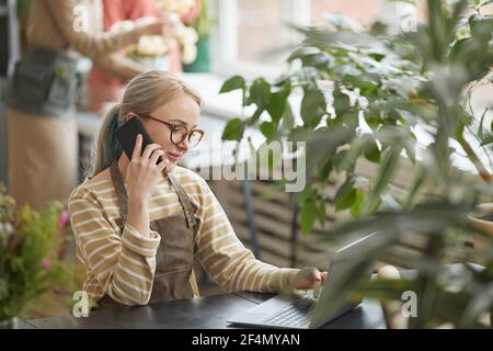 Vista laterale ritratto di giovane donna d'affari che parla per telefono in negozio di fiori mentre gestisce piccola impresa, spazio di copia Foto Stock