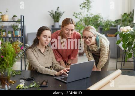 Ritratto di tre giovani donne che usano il laptop in negozio di fiori mentre si gestisce la piccola impresa, copia spazio Foto Stock