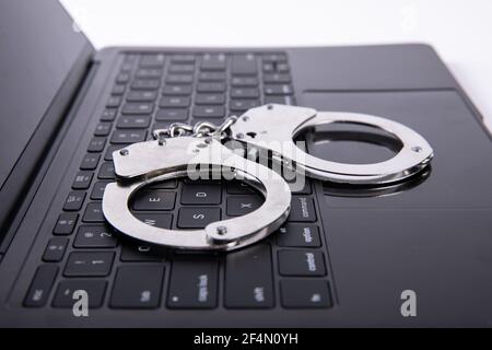 Foto closeup di manette poggiate sulla tastiera del computer portatile - online concetto di criminalità Foto Stock