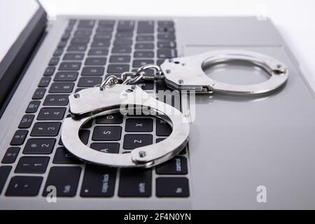 Foto closeup di manette poggiate sulla tastiera del computer portatile - online concetto di criminalità Foto Stock