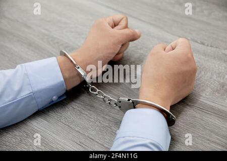 Colpo di closeup di mani maschili in manette su un legno tabella Foto Stock