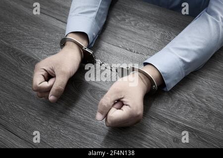 Colpo di closeup di mani maschili in manette su un legno tabella Foto Stock