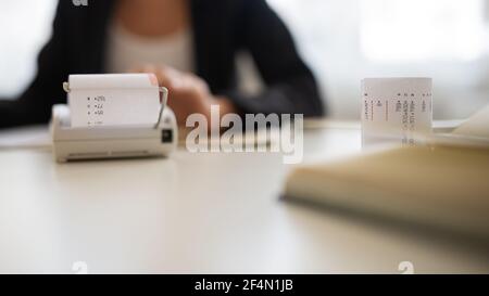 Visualizzazione ad angolo basso di un contabile che utilizza l'aggiunta di una macchina con la stampa che ne esce. Foto Stock