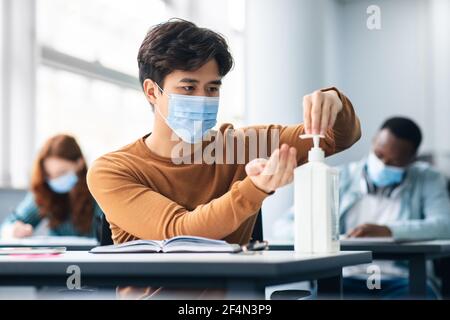 Studente asiatico maschio che applica l'igienizzatore antibatterico sulle mani Foto Stock