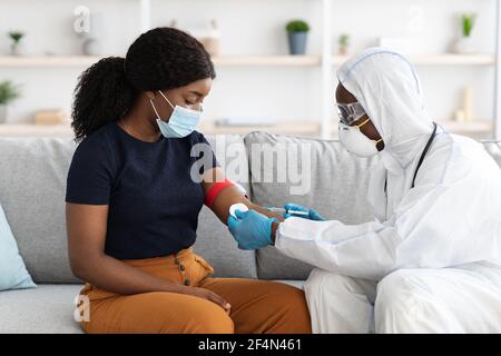 Medico in tuta protettiva che preleva il campione di sangue per la paziente femminile Foto Stock